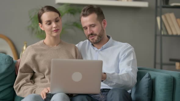Couple Working on Laptop Together While Sitting on Sofa alt