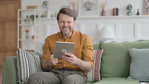 Young Man Celebrating Success on Tablet on Sofa alt
