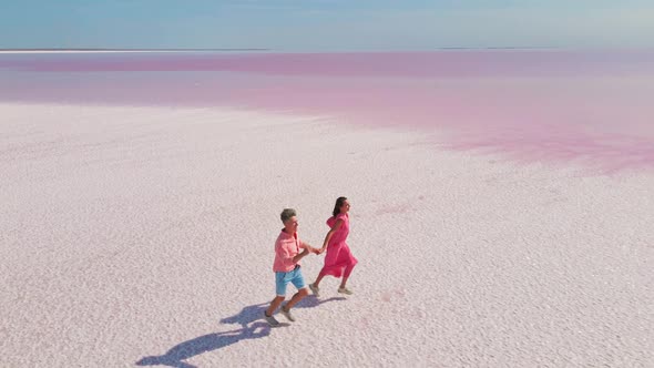 Aerial Drone Footage of Happy Young Couple in Pink Wear Having Fun and Joyfully Running on White alt