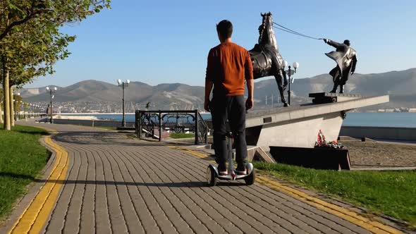 A Man is Riding Segway at the City on Seafront Rear View