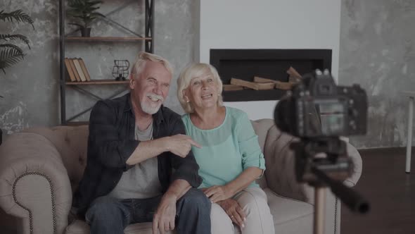 Technology, Blogging and People Concept - Happy Smiling Senior Couple with Camera Recording Video alt