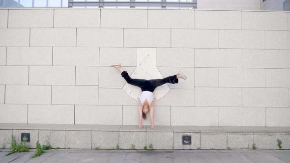 Woman doing a handstand and moving legs in front of wall alt