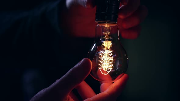 A man twists in a decorative light bulb and it lights up in the dark copy space