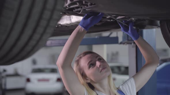 Camera Moving From Left To Right Around Young Caucasian Woman Standing Under Car and Tightening alt