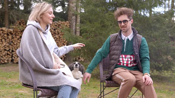 Happy Friends with Dog Enjoying Camping, Sitting By Fire Chating Outdoors