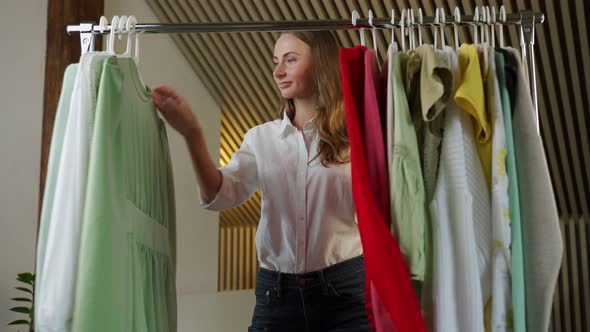 Beautiful Thoughtful Woman Stylist Chooses Clothes on a Hanger in the Dressing Room alt
