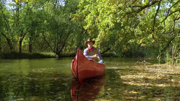 Cowboy in a Canoe Floats on the River in the Forest alt