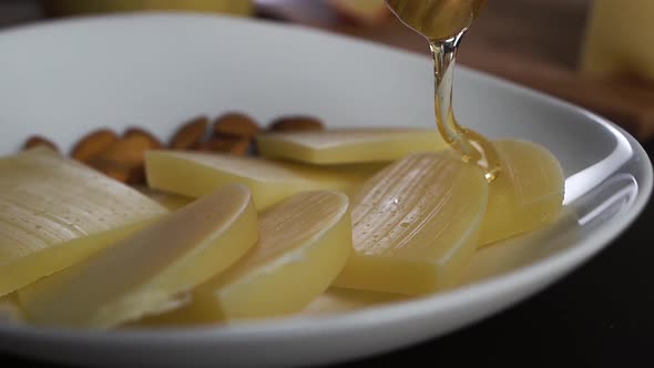 Spoonful of Honey Pours Thick Stream on the Sliced ​​Hard Cheese on Plate