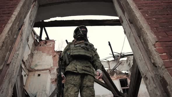 A Soldier in Professional Equipment with Rifle Inspects the Ruins of a House Destroyed By War