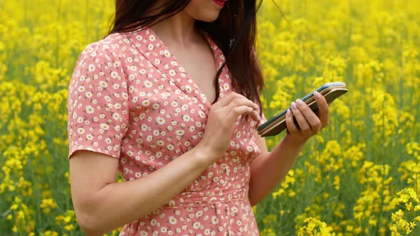A beautiful cheerful young girl takes pictures of herself on the phone in a field alt