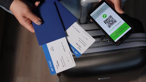 A Woman Holding a Phone with a QR Code and Passports with Tickets at the Airport alt