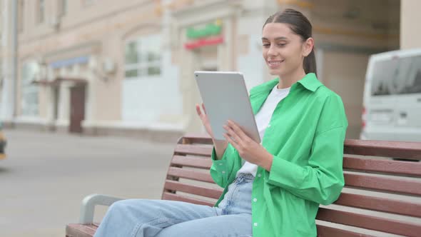 Hispanic Woman Using Tablet While Sitting Outdoor on Bench alt