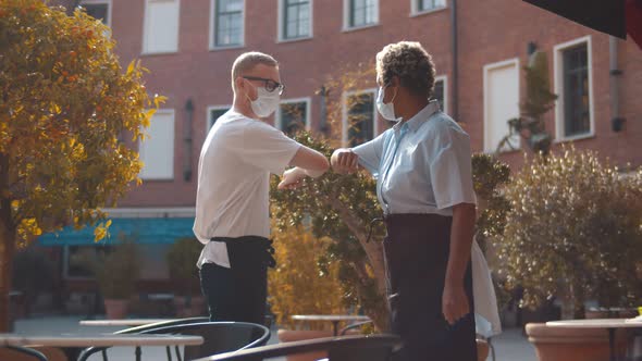 Diverse Waiters in Safety Mask Greeting Touching Elbows Standing Outdoors Cafe alt