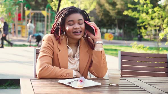 African American Woman Sitting in Outdoor Cafe and Talking on the Phone