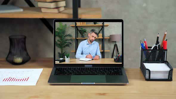 Laptop Standing on Table Display with Businessman in Office Writes in Notebook alt