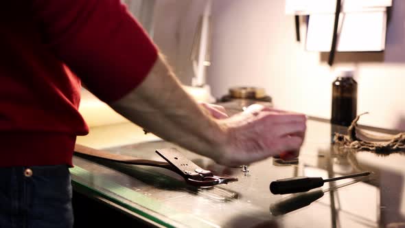 Leather Workshop  a Man Screws a Buckle to a Leather Belt Using a Screwdriver alt