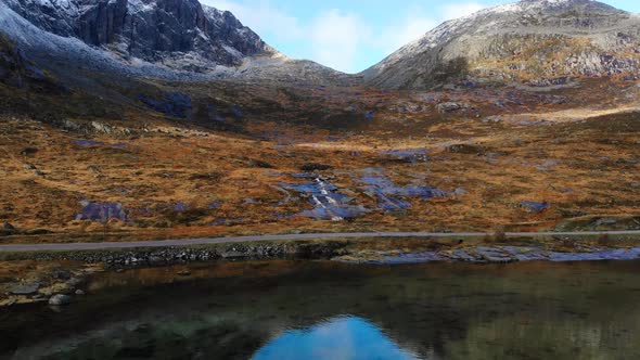 Droneshot of norway and a waterfall in the mountains next to a street. alt