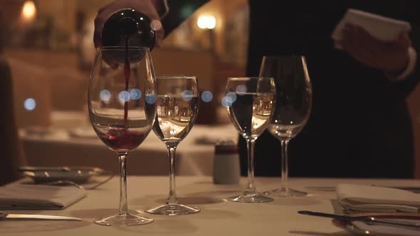 Slow motion shot of waiter pouring wine in glass at restaurant - customer taking glass and drinking alt