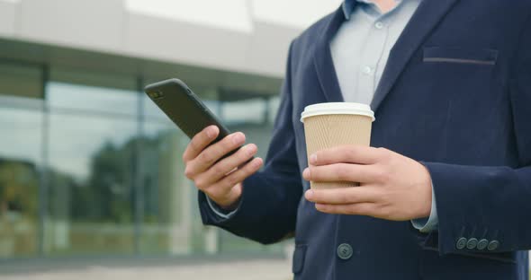 A Businessman Stands Outside the Business Center with a Cup of Coffee in His Hand alt