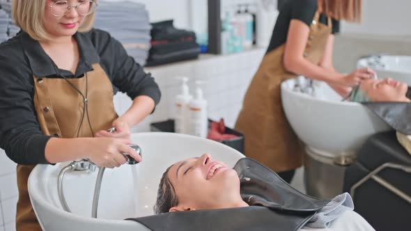 Asian young woman lying down on salon washing bed getting hair washed in hair salon by stylist. alt