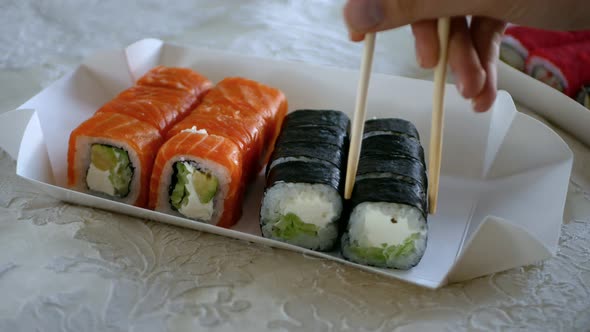 Beautiful Female Hand Carefully Takes Sushi Roll with Wooden Chopsticks