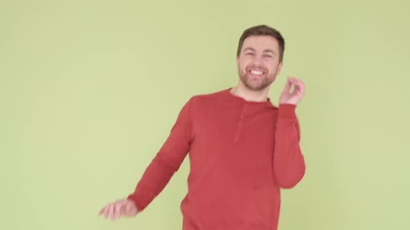 Cheerful Smiling Young Man in Orange Sweater Funny Dancing on Yellow and Green Background alt