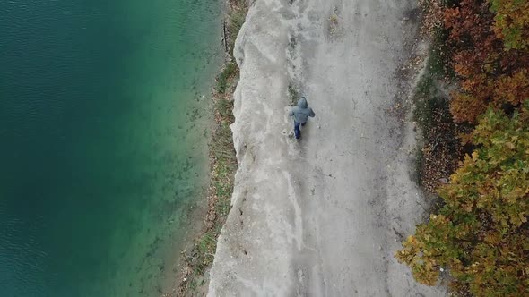 Man walking along lake. Aerial view of man walking along lake with forest alt