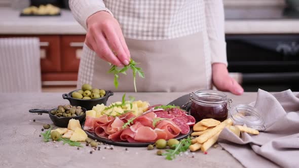 Making Meat and Cheese Antipasto Plater Woman Pouring Arugula to Serving Board with Cheese alt