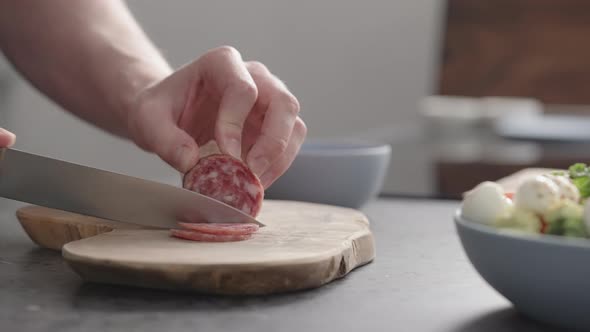 Slow Motion Man Slicing Salame on Olive Wood Board on Concrete Countertop alt