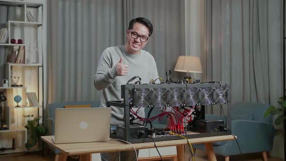 Smiling Asian Man Showing Thumbs Up While Using Laptop And Mining Rig For Mining Cryptocurrency alt