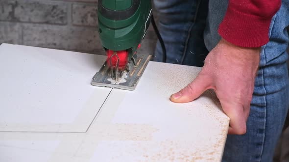 A Man Cuts a Window Sill From Board for a Window Using an Electric Jigsaw for Work