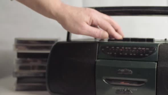 Hand ejecting retro cassette tapes into radio cassette player wide shot alt