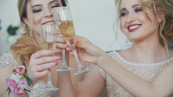 20s Girls Sit on Couch at Home and Drink Champagne From Glasses alt