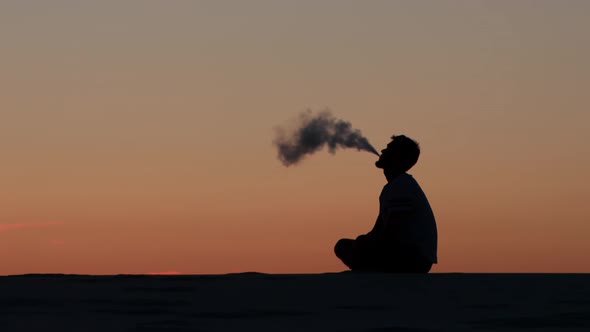 Guy Holds an Electronic Cigarette in His Hand and Smokes It. Silhouette alt