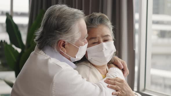 Two elderly Asian couples wearing masks hug and encourage each other.