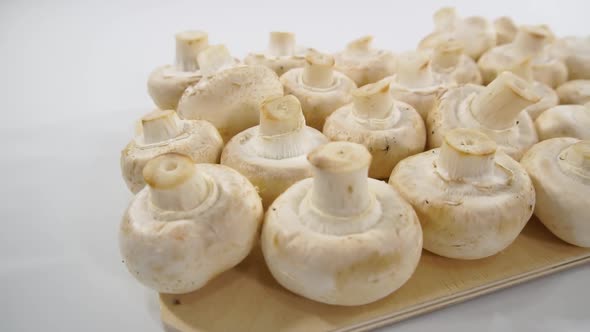 Champignon mushrooms on a wooden cutting board. Dolly shooting, white background.