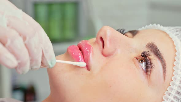The Cosmetologist Applies Soothing Lip Balm to the Lips with a Cotton Swab