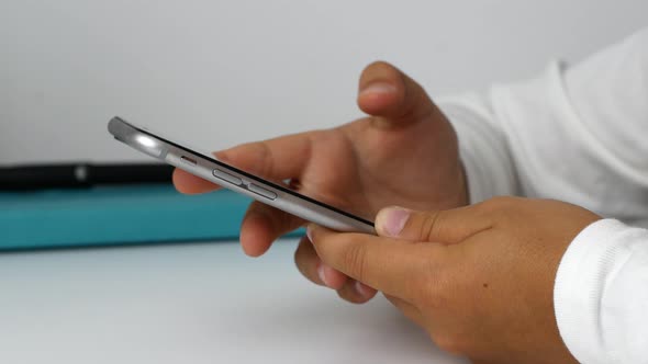 A child girl holds a phone in her hands, sits at the table, and does her homework. alt