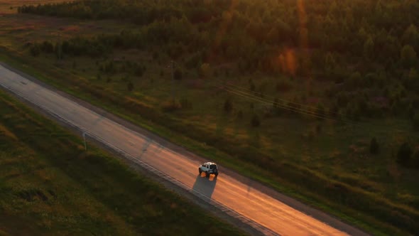 Aerial View of a Car Driving on the Road at Sunset alt