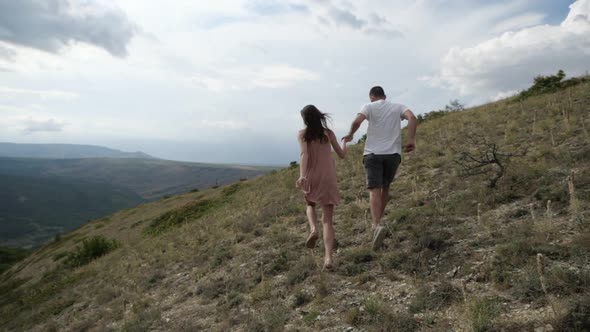 Young Couple Runs Through the Valley Amid Mountains and Clouds
