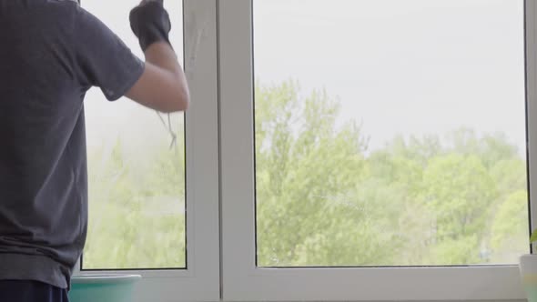 Man washes the windows with special foam and cleans them. Cleaning service. Worker in black gloves alt