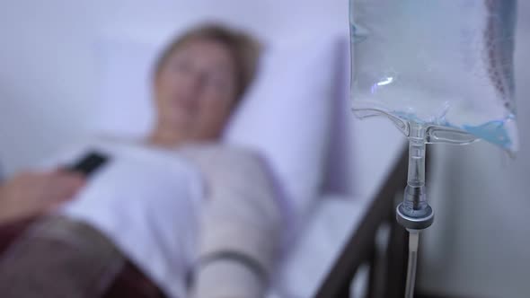 Drop Counter Close-Up, Mature Female Patient Sleeping in Sickbed With Phone alt