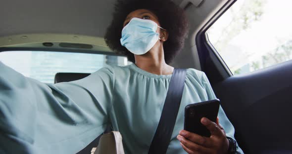 African american businesswoman with face mask using smartphone alt