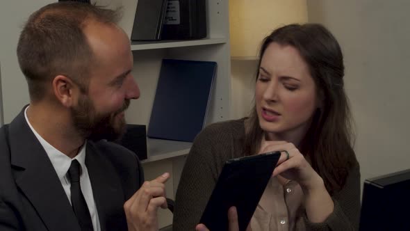 Businessman and businesswoman talk about paperwork and data on a tablet computer. alt
