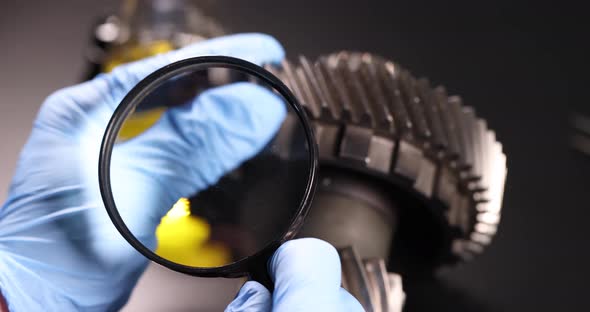 Master Repairman Looks Through a Magnifying Glass at the Differential of the Car alt