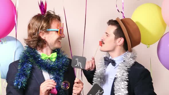 Two cheerful guys holding sign in love in photo booth alt