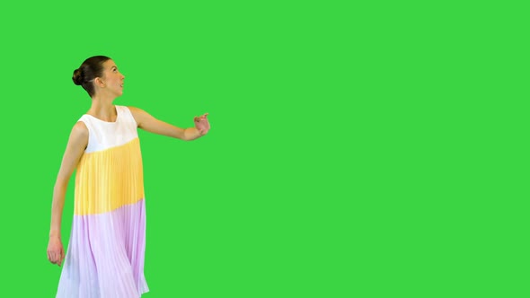 Young Beautiful Girl in Whiteyellow Dress Walks in Artistic Manner Looking Around on a Green Screen