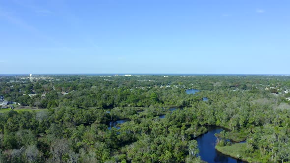 Lowering Aerial of a River Flowing Through Forest and Towards a Suburban Town alt