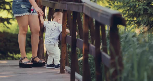 Kid Stands on a Wooden Bridge with His Mother and Looks Down alt