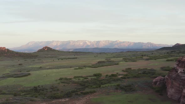 Wide slow tracking drone over grassy field with far off mountains in the distance alt